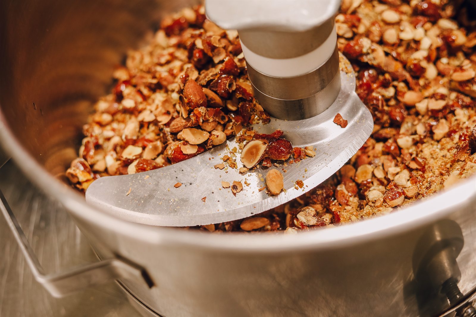 Une lame concasse les amandes caramélisées dans une cuve en inox